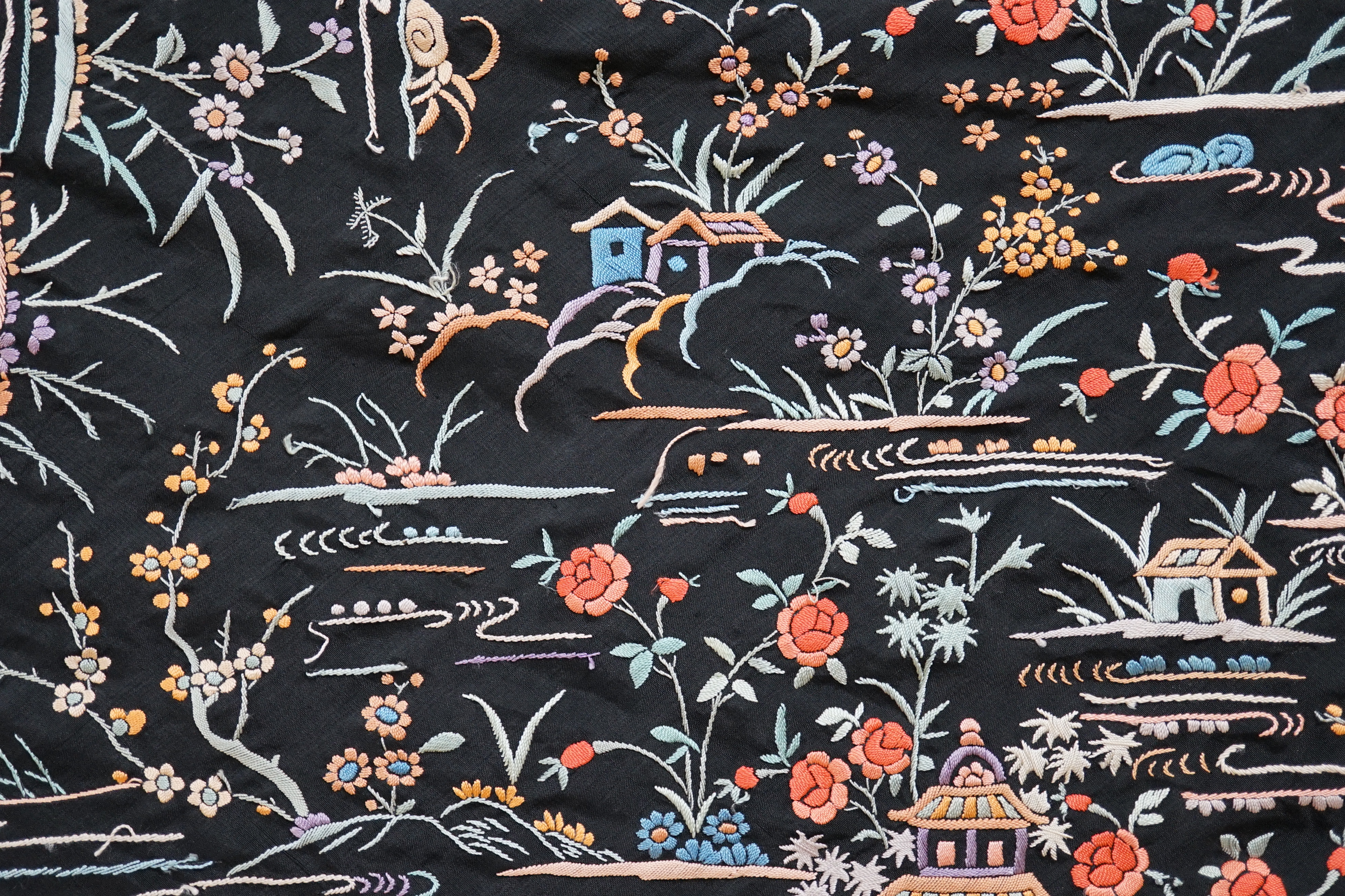 An early 20th century Chinese black silk shawl, with all over coloured floral embroidery, embroidered with multi-coloured silks and a long silk fringe, unusually the four corners are embroidered with a figurative pagoda